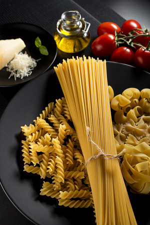 Raw mixed pasta with ingredients on black background.の写真素材