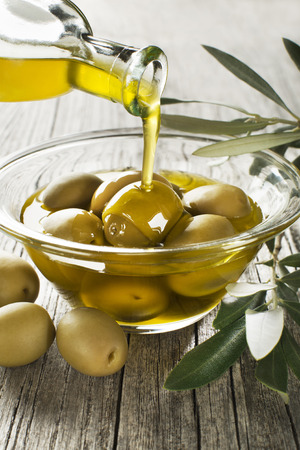 Bottle pouring virgin olive oil in a bowl with green olives close upの写真素材
