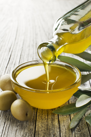Bottle pouring virgin olive oil in a bowl close upの写真素材