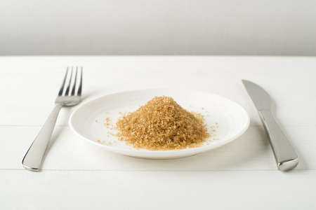 Junk-food, diet and unhealthy eating concept - close up of sugar on plate with knife and fork.の写真素材