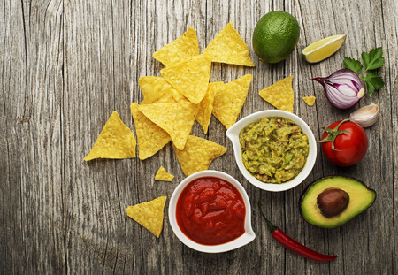 Avocado guacamole and tomato salsa with fresh ingredients on tableの写真素材