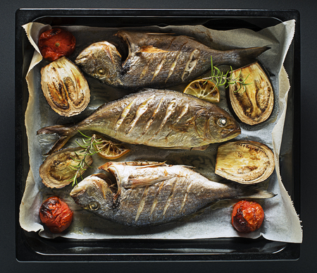 Grilled Gilt-head bream fish with lemon, herbs, oil, vegetables and spicesの写真素材