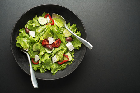 Green salad with cheese and fresh vegetables on a black background. Greek salad.の写真素材