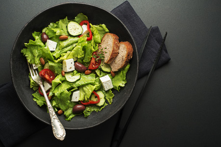 Green salad with cheese and fresh vegetables on a black background. Greek salad.の写真素材