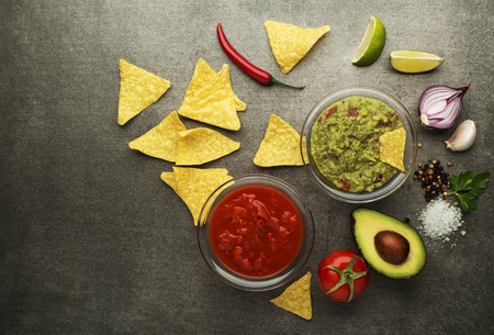Avocado guacamole and tomato salsa with fresh ingredients on tableの写真素材