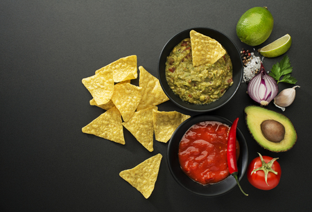 Avocado guacamole and tomato salsa with fresh ingredients on tableの写真素材