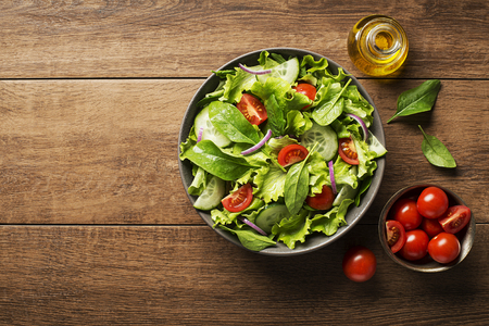 Green salad with tomato and fresh vegetables on a wooden backgroundの写真素材