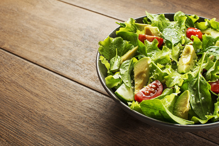 Green lettuce salad with avocado and fresh vegetables on wooden background.の写真素材