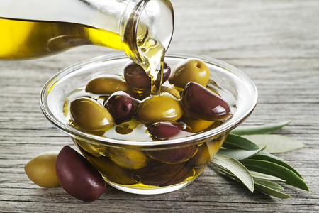 Bottle pouring virgin olive oil in a bowl with olives close upの写真素材
