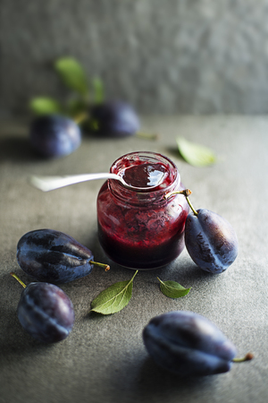 Plum jam or marmalade in a glass jar with plums fruit aroundの写真素材