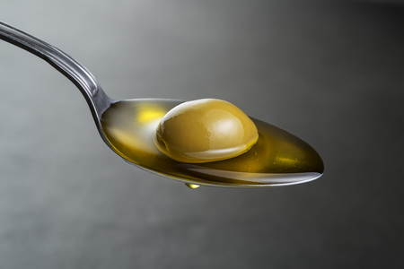 Spoon of virgin olive oil and green olive close upの写真素材