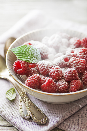 Raspberry berries with green leaf sprinkled with sugar close up. Healthy dessert with fresh fruit.の写真素材