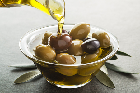 Organic olive oil. Bottle of Extra virgin oil pouring in to glass bowl with olivesの写真素材