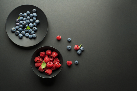 Fresh blueberries and raspberries in a bowl on black backgroundの写真素材