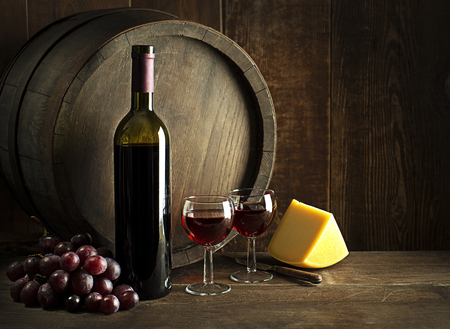 Bottle of red wine with glasses and cheese on wooden and barrel background.の写真素材