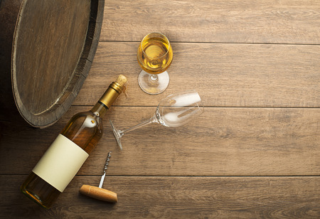 Bottle of white wine with label on old board. Wine bottle and glass with barrel backgroundの写真素材