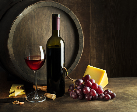 Bottle of red wine with glass and cheese on wooden and barrel background.の写真素材