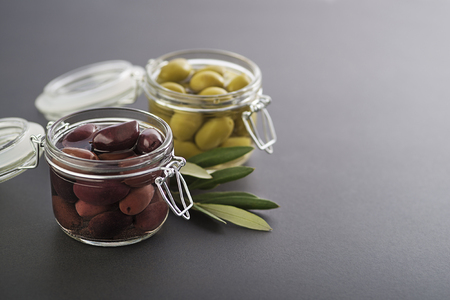 Pickled green and black olives in glass jar with branch leavesの写真素材