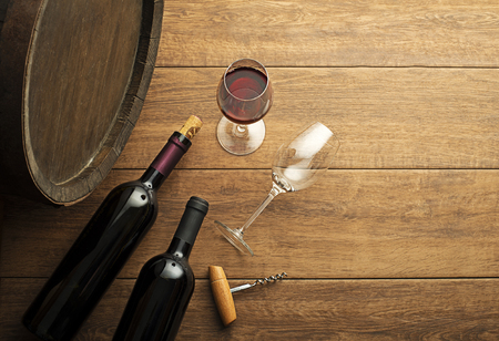 Glass and bottle of red wine with wooden and barrel backgroundの写真素材