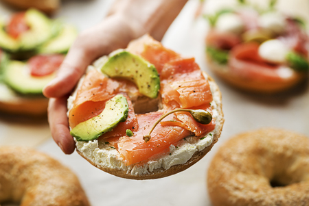 Woman is holding a Bagel with cream, avocado and smoked salmon. Healthy breakfast food.の写真素材