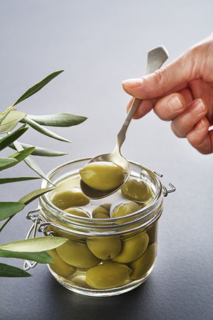 Pickled green olives in glass jar close up. Eating with spoon.の写真素材