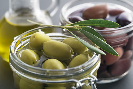 Pickled green and black olives in glass jar with branch leaves close upの写真素材