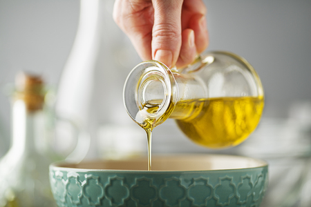 Bottle of virgin olive oil pouring to bowl close upの写真素材