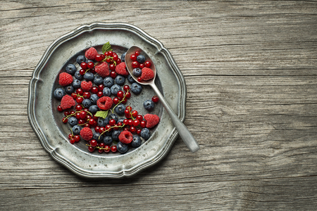 Mix of fresh berries in a plate with spoon on wooden backgroundの写真素材