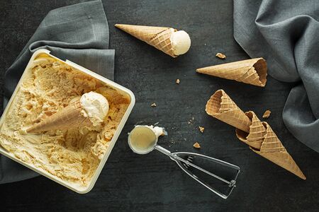 Vanilla ice cream scoops, scooped from container in to waffle cones with a silver utensilの写真素材