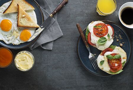 Breakfast served with coffee, jam, butter, mozzarella sandwich and fried eggs with bread on dark table top view. Heathy breakfast food.の写真素材