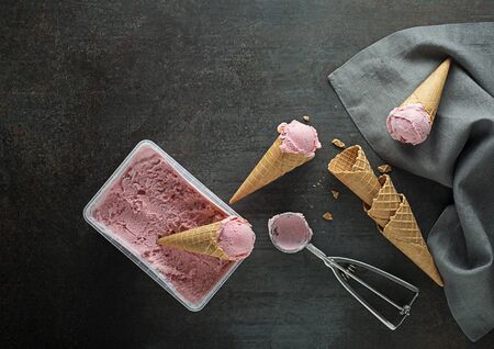 Fresh of soft ice cream or frozen yogurt with berry fruit flavours. Fruit ice cream scoops, scooped out of container in to waffle cones with a silver utensilの写真素材