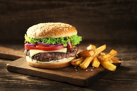 Delicious Hamburger with cheese and french fries on wooden table and darkの写真素材