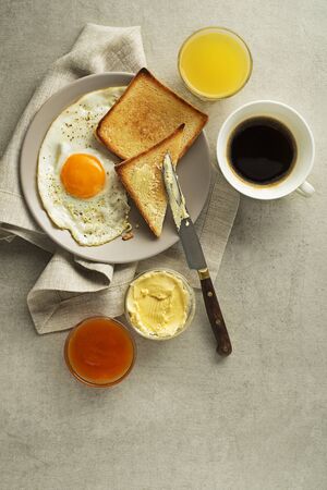 Breakfast served with fried egg, jam, butter, coffee and juice on the table top view.の写真素材