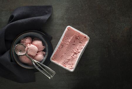 Fresh of soft ice cream or frozen yogurt with berry fruit flavours. Fruit ice cream scoops, scooped out of container with a silver utensilの写真素材
