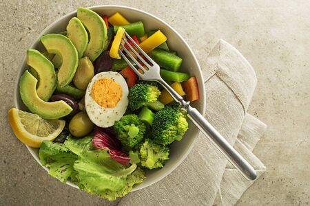 Healthy Green salad with avocado, egg and fresh vegetables on grey table backgroundの写真素材