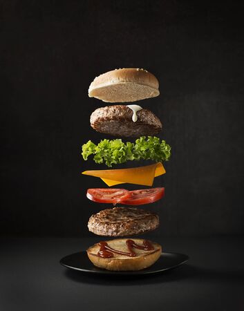 Maxi hamburger with flying ingredients placed on black background. Conceptual jumping Burger. Delicious and attractive hamburger with refreshing ingredientsの写真素材