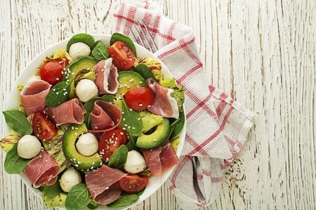 Healthy green salad with prosciutto, avocado and mozzarella cheese on wooden table background. Healthy meal.の写真素材
