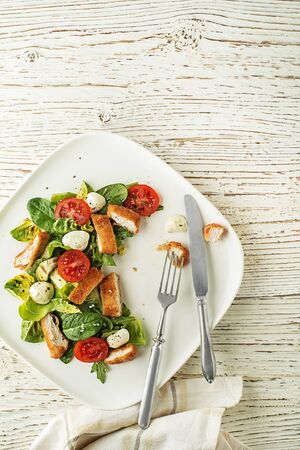 Healthy green salad with crispy fried breaded chicken breast strips and mozzarella on white backgroundの写真素材