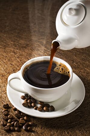 Coffee pot pouring fresh hot coffee into cup on dark backgroundの写真素材