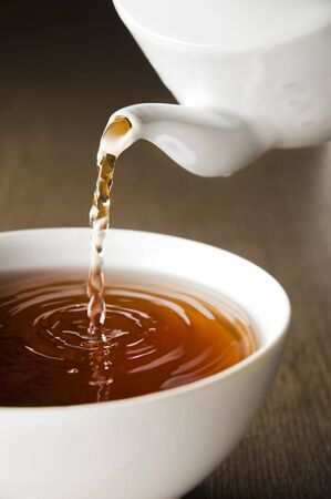 Teapot pouring fresh hot tea in to Cup, on dark background. The Time of Tea Break.の写真素材