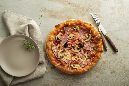 Pizza served with mozzarella cheese, ham, mushrooms and tomato sauceの写真素材