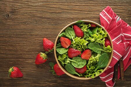 Healthy green salad with fresh strawberry fruit on wooden table background. Healthy salad meal.の写真素材