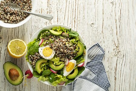 Healthy green salad meal with quinoa, egg and avocado on wooden backgroundの写真素材