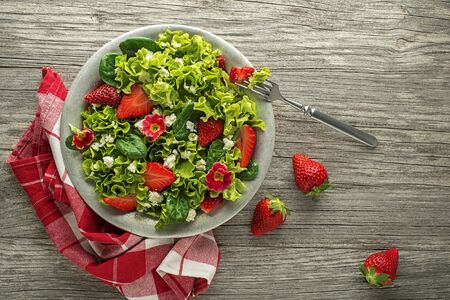 Healthy green salad with strawberry and fresh cheese on wooden table background. Healthy salad meal.の写真素材