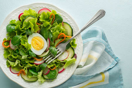 Healthy Green salad with fresh vegetables and boiled egg on blue table backgroundの写真素材
