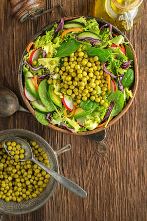 Green lettuce salad with fresh vegetables and cooked peas on wooden table backgroundの写真素材