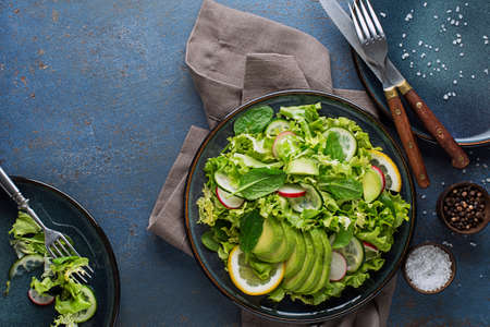 Green salad with avocado and fresh vegetables on a blue backgroundの写真素材