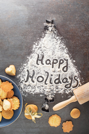 Making and baking cut-out sugar cookies of all shapes and sizes. Holiday, celebration and cooking concept. Happy Holidays written with flourの写真素材