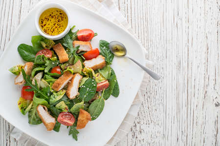 Healthy green salad with crispy fried breaded chicken breast strips and tomatoes.の写真素材