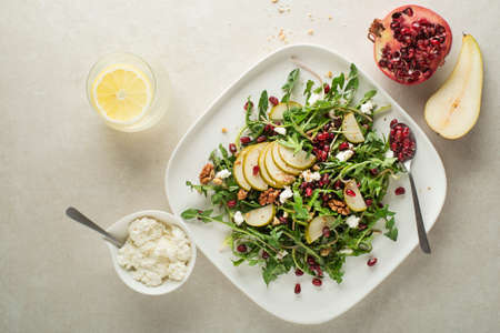 Healthy dandelion salad with pear fruit, pomegranate and fresh cheese on grey backgroundの写真素材
